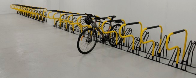 One bike is parked in a row of yellow ground mounted bike parking rails.